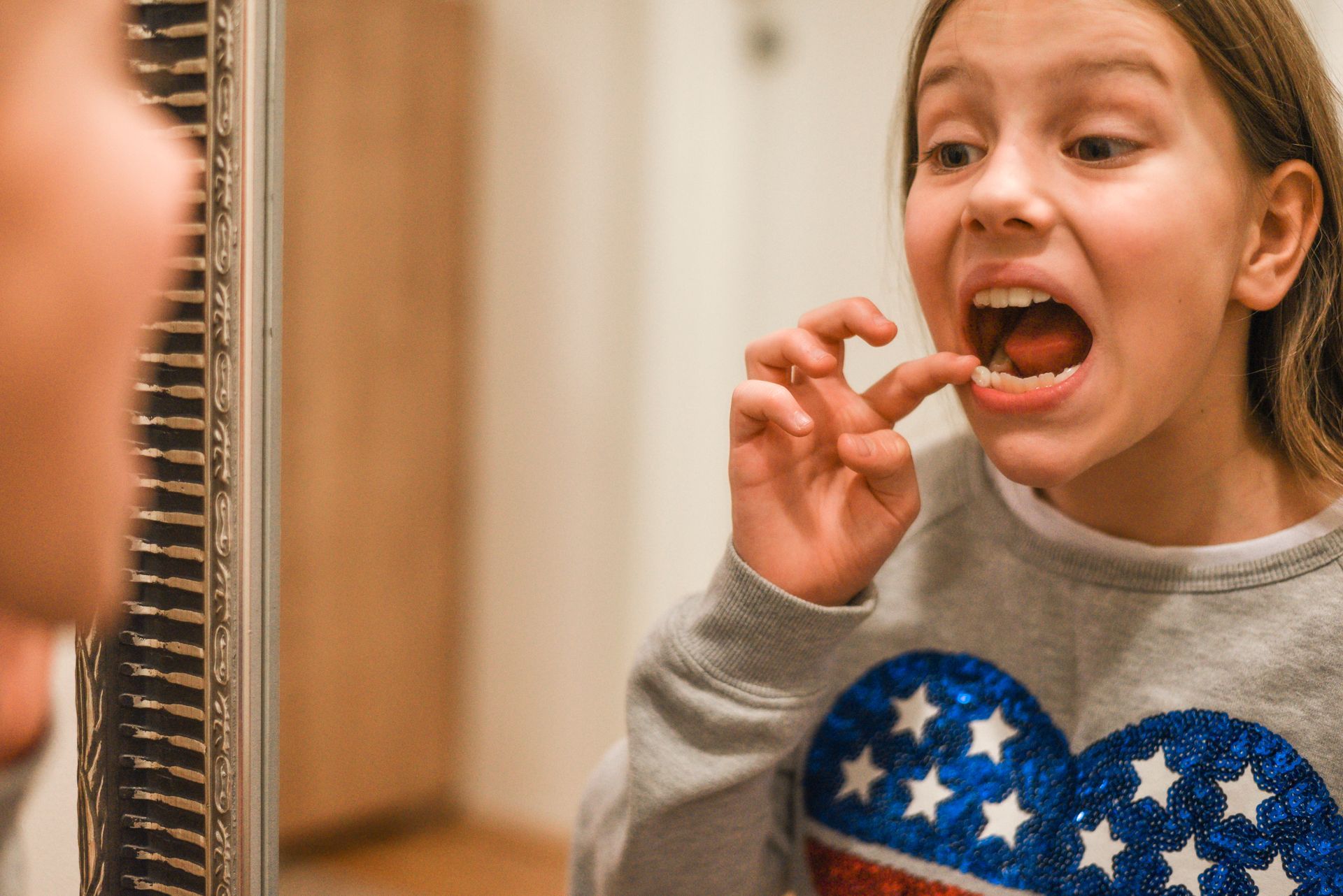 A young girl is brushing her teeth in front of a mirror.