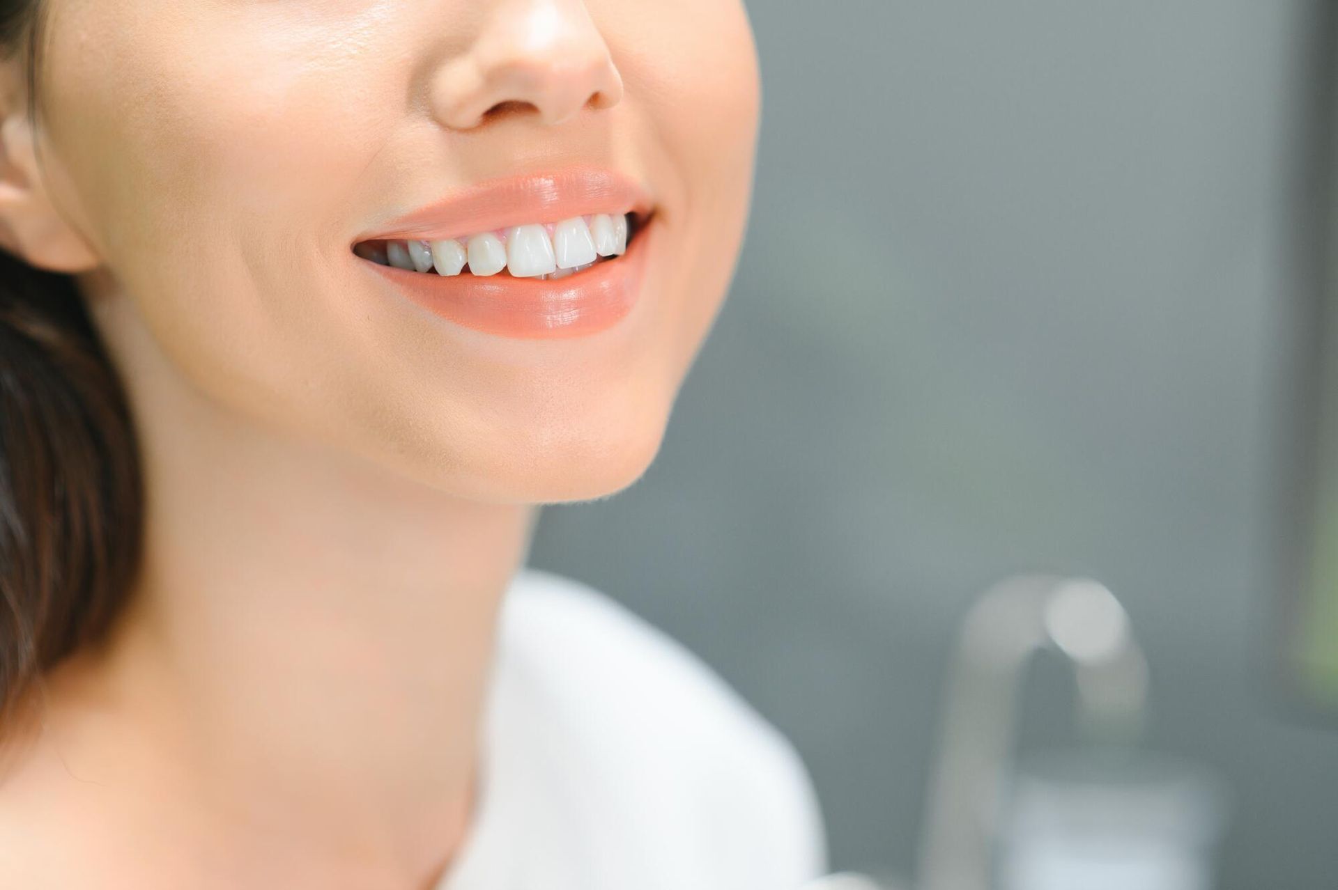 A close up of a woman 's face with white teeth smiling in front of a mirror.