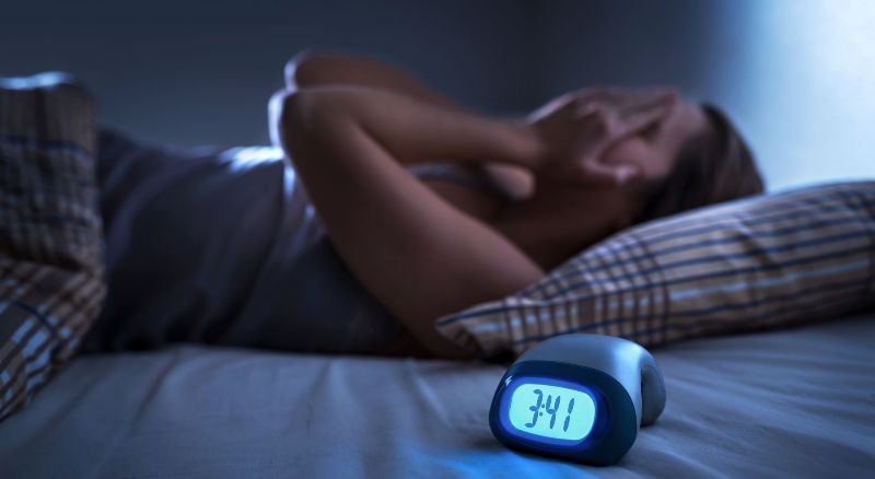 A woman is laying on a bed next to an alarm clock that says 3:41