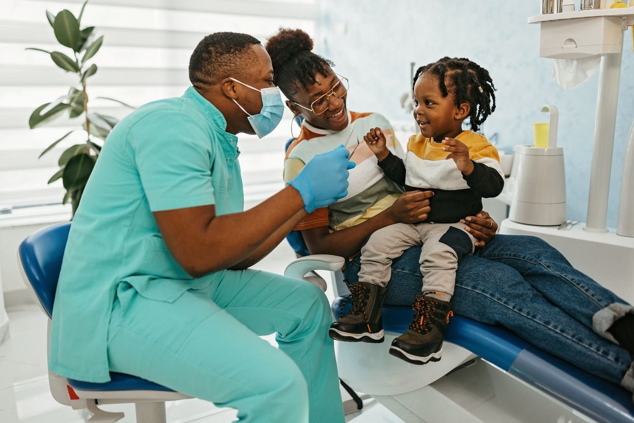 A dentist is talking to a woman and child in a dental chair.