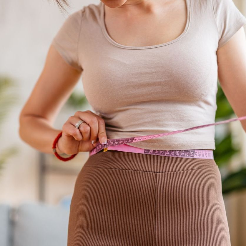 A woman is measuring her waist with a tape measure