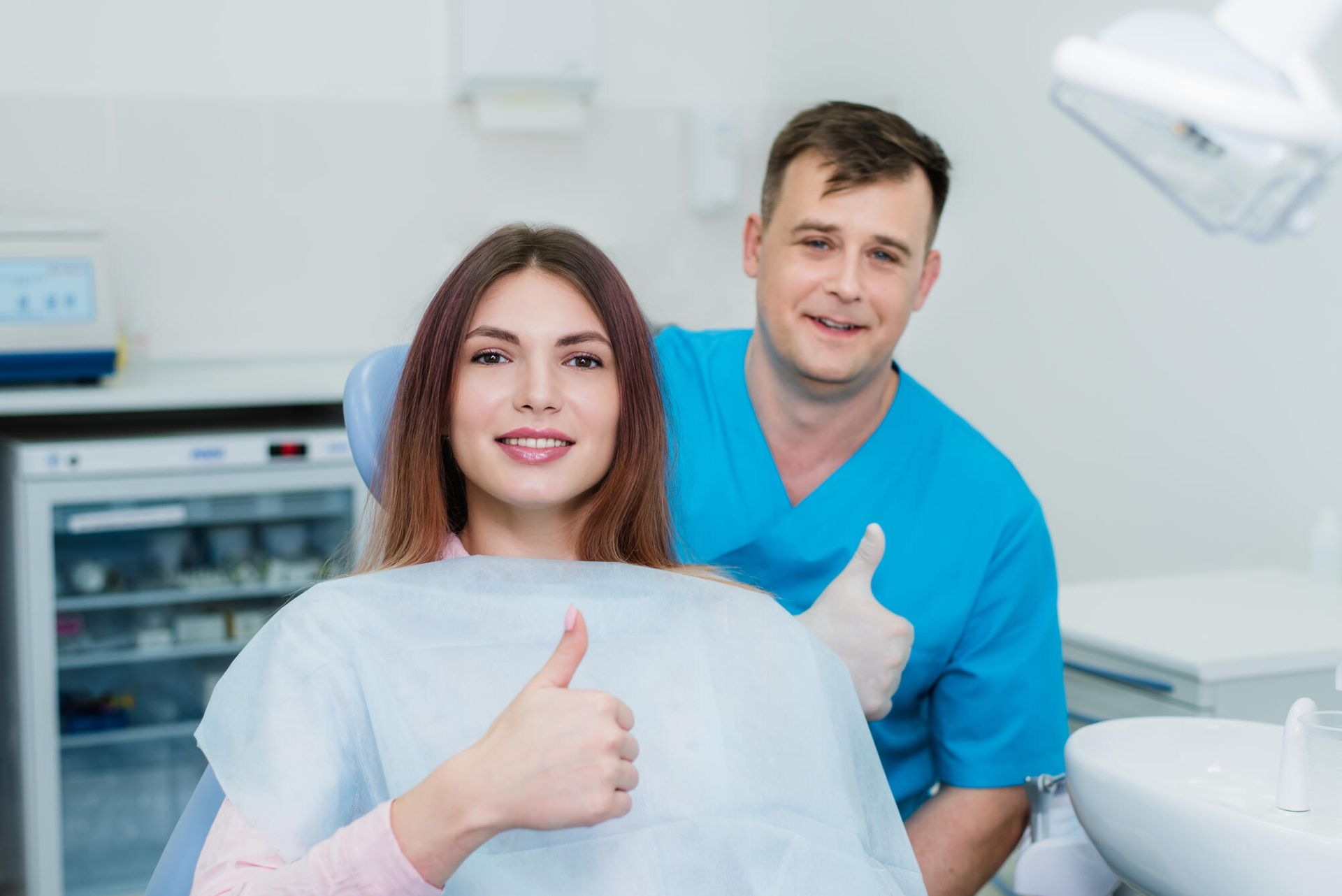 Woman in dental chair gives thumbs up, with dentist smiling and giving thumbs up.