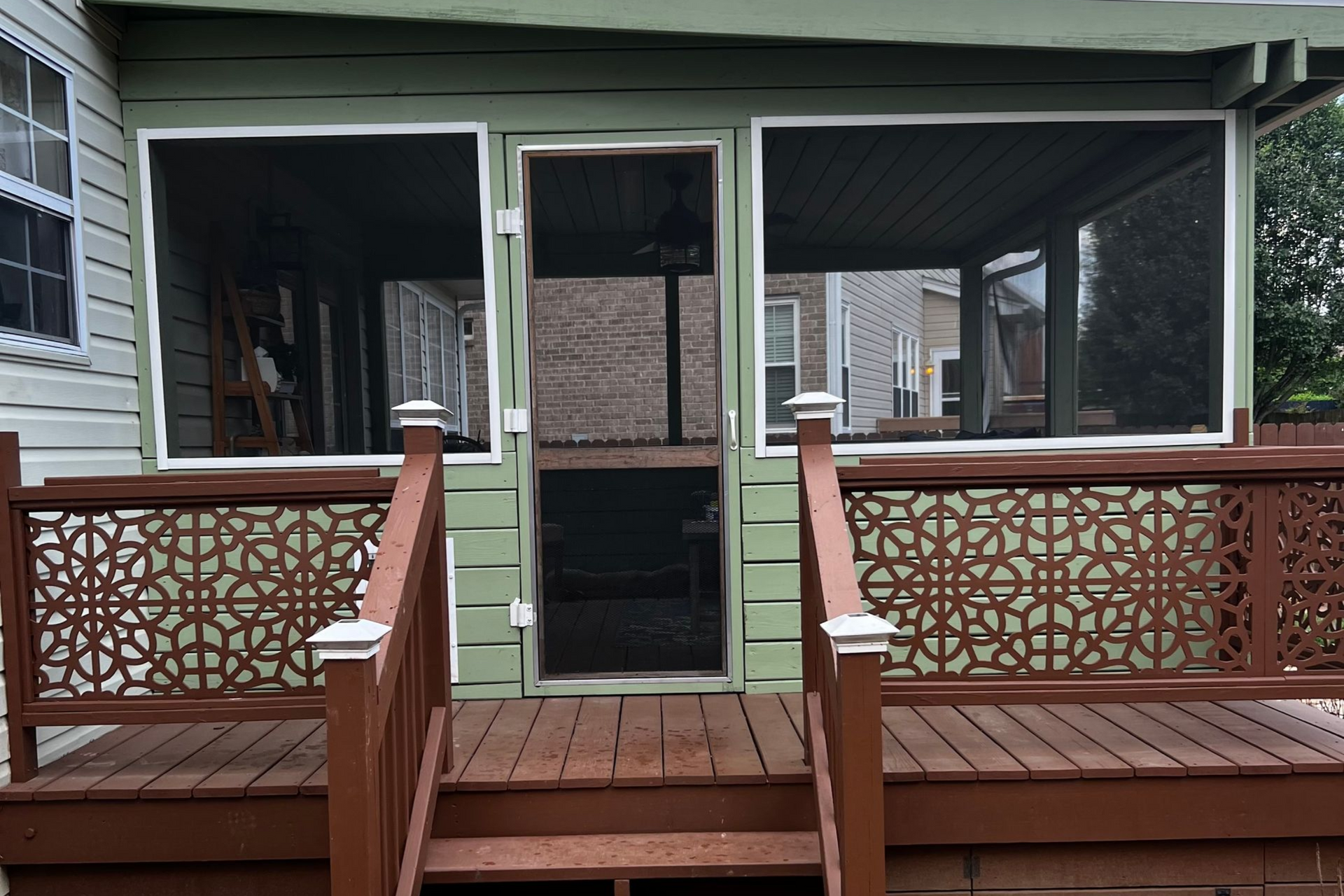 Wooden deck with steps, table, chairs, potted plants, and brick house.