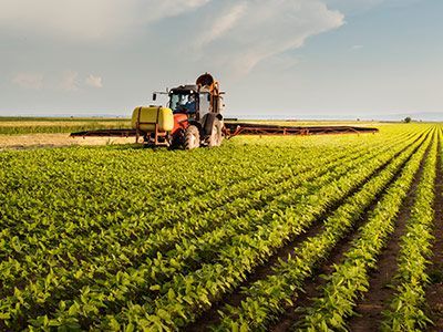 Tractor spraying crops in a green field under a partly cloudy sky.