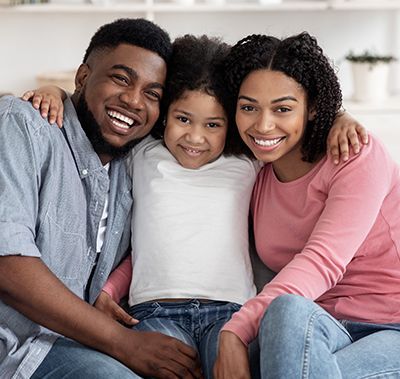 Family of three smiles at the camera, arms around each other.