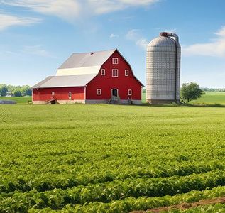 A red barn sits in the middle of a green field next to a silo.