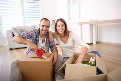 Couple packing cardboard boxes in a bright room, smiling.