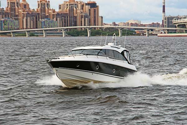 Motorboat speeding across water in front of a city skyline and bridge.