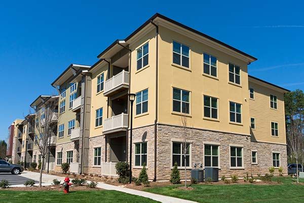 Multi-story apartment building with yellow stucco, stone facade, and balconies. Blue sky.