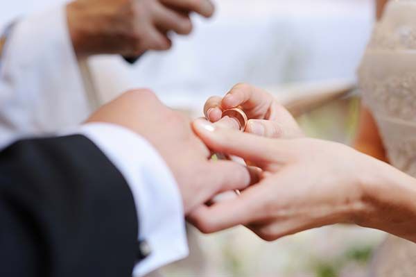 Bride putting a wedding ring on groom's finger during a ceremony.