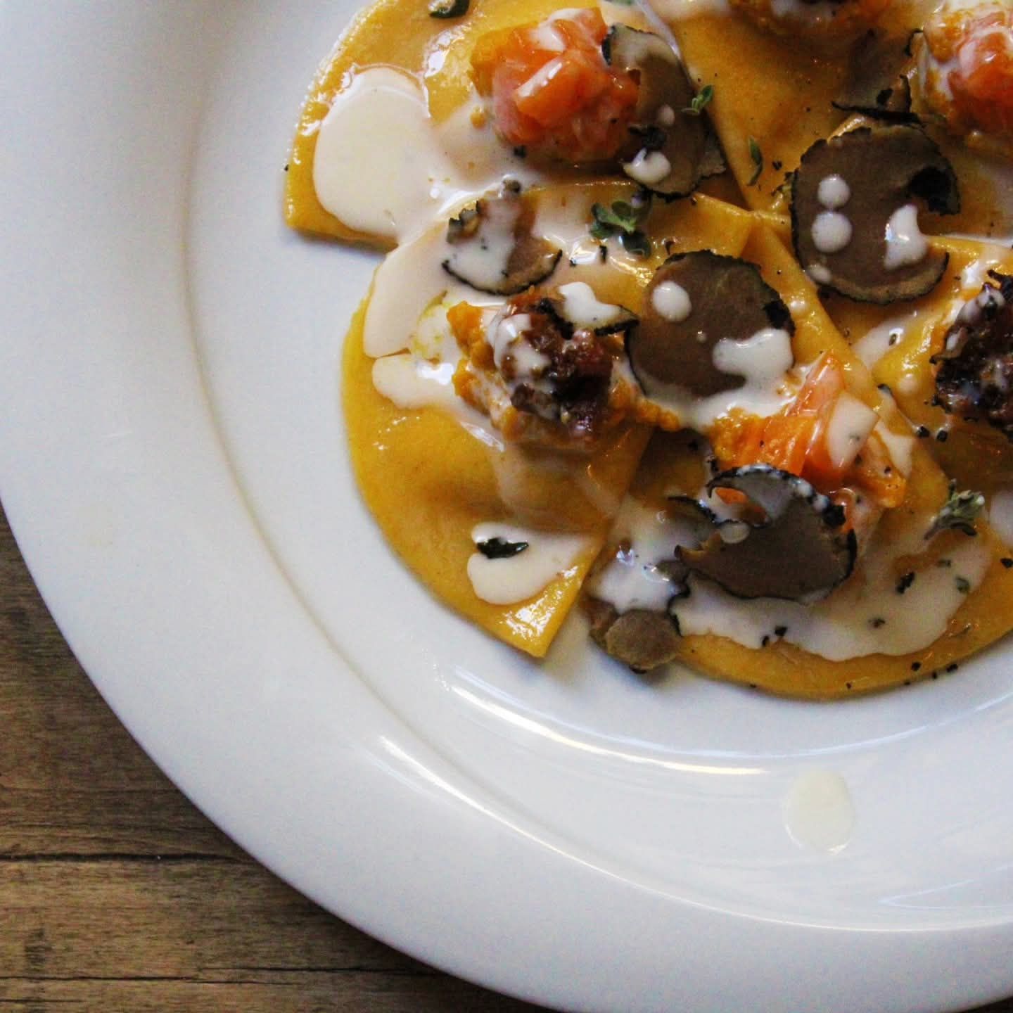 Piatto di pasta con pasta gialla, salsa alla panna, tartufi e pomodori su un piatto bianco.