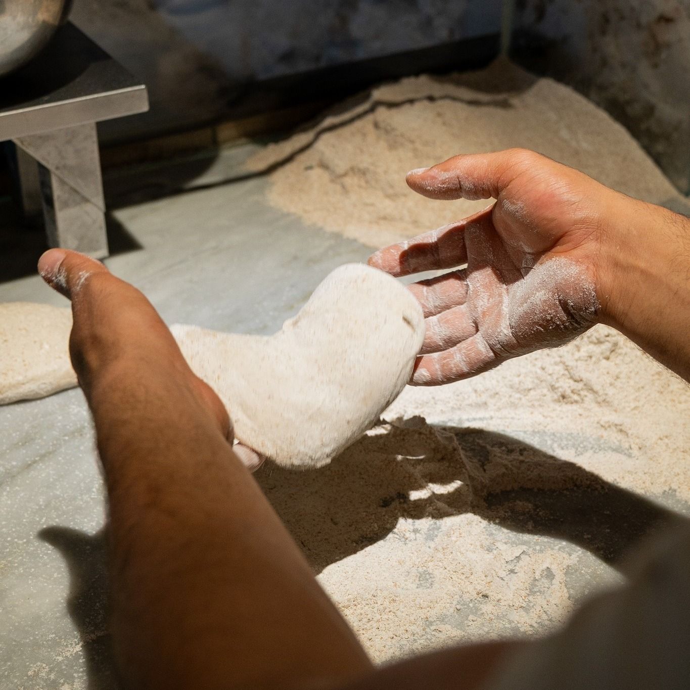 Mani che modellano l'impasto su una superficie infarinata in un panificio.