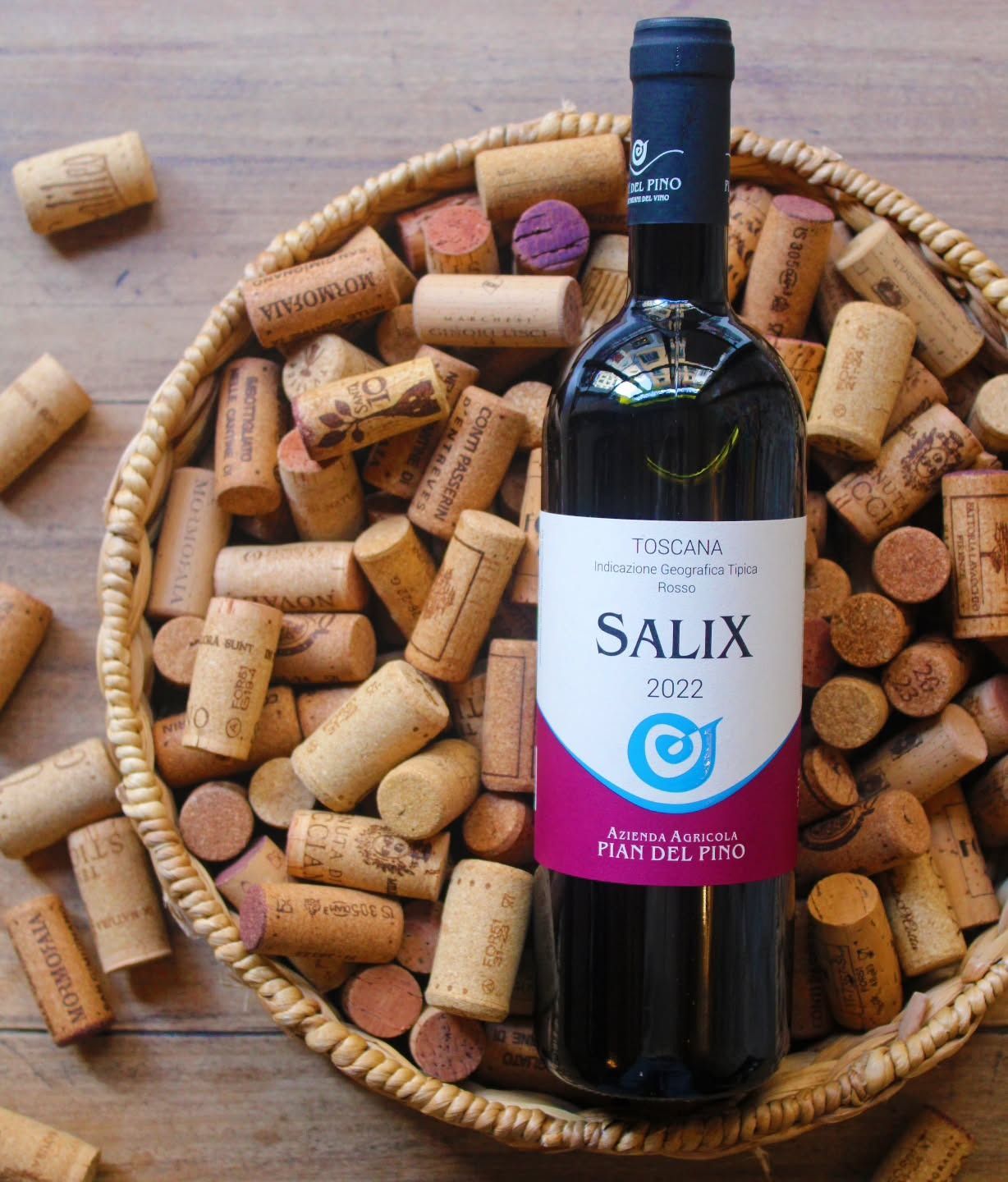 Bottiglia di vino rosso "Salix" circondata da tappi di sughero in un cesto intrecciato.