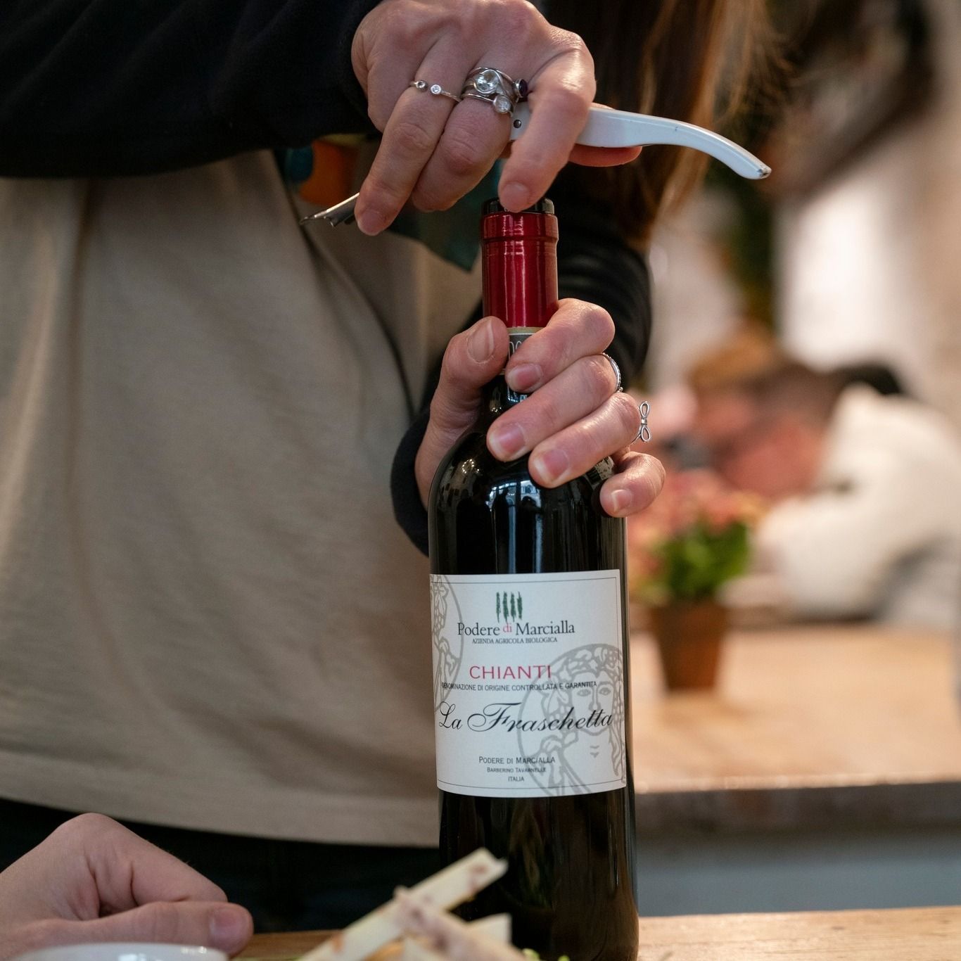 Persona che apre una bottiglia di vino rosso con un cavatappi.