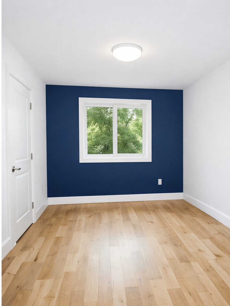 Empty room with hardwood floors, white walls, a navy blue accent wall with a window, and a white door.