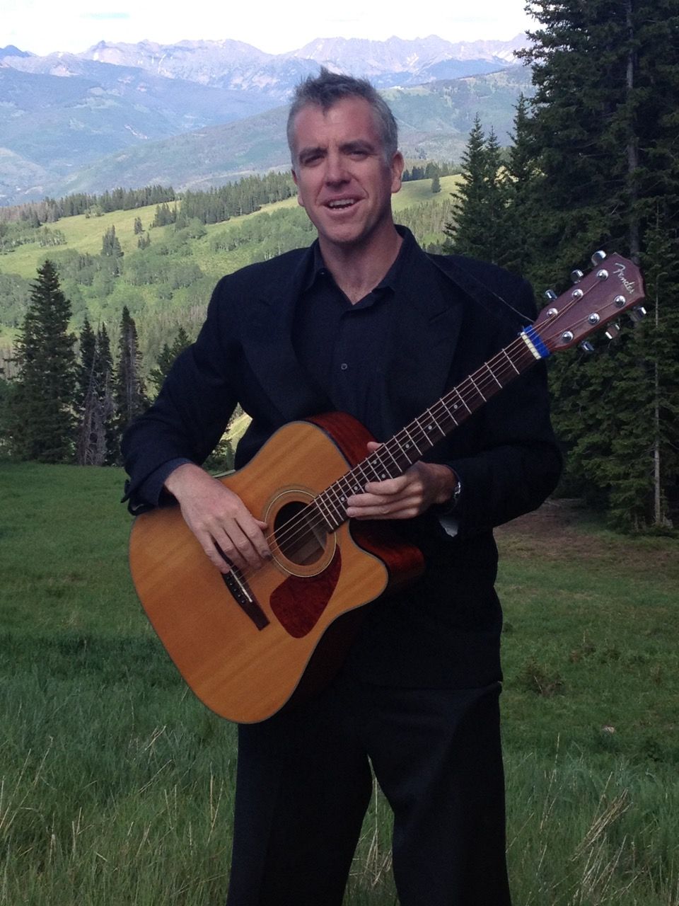Jonny Mogambo standing with guitar in front of mountain