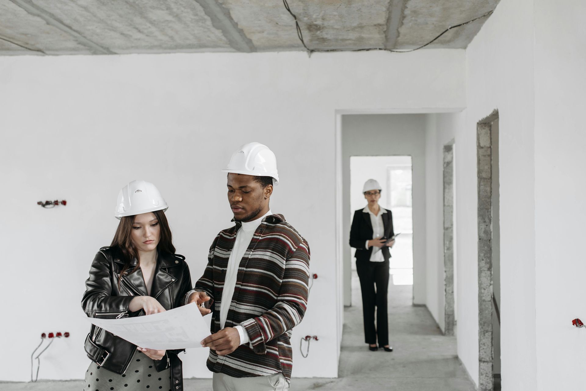 Two construction workers in hard hats reviewing a floor plan in a white room under renovation