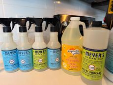 Bottles of cleaning products on a countertop, including spray bottles of Meyer's and a larger container of lemon cleaner.