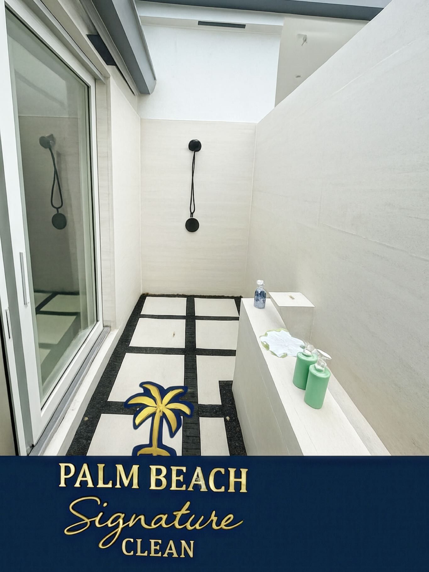 Outdoor shower with palm tree mat and cleaning supplies.
