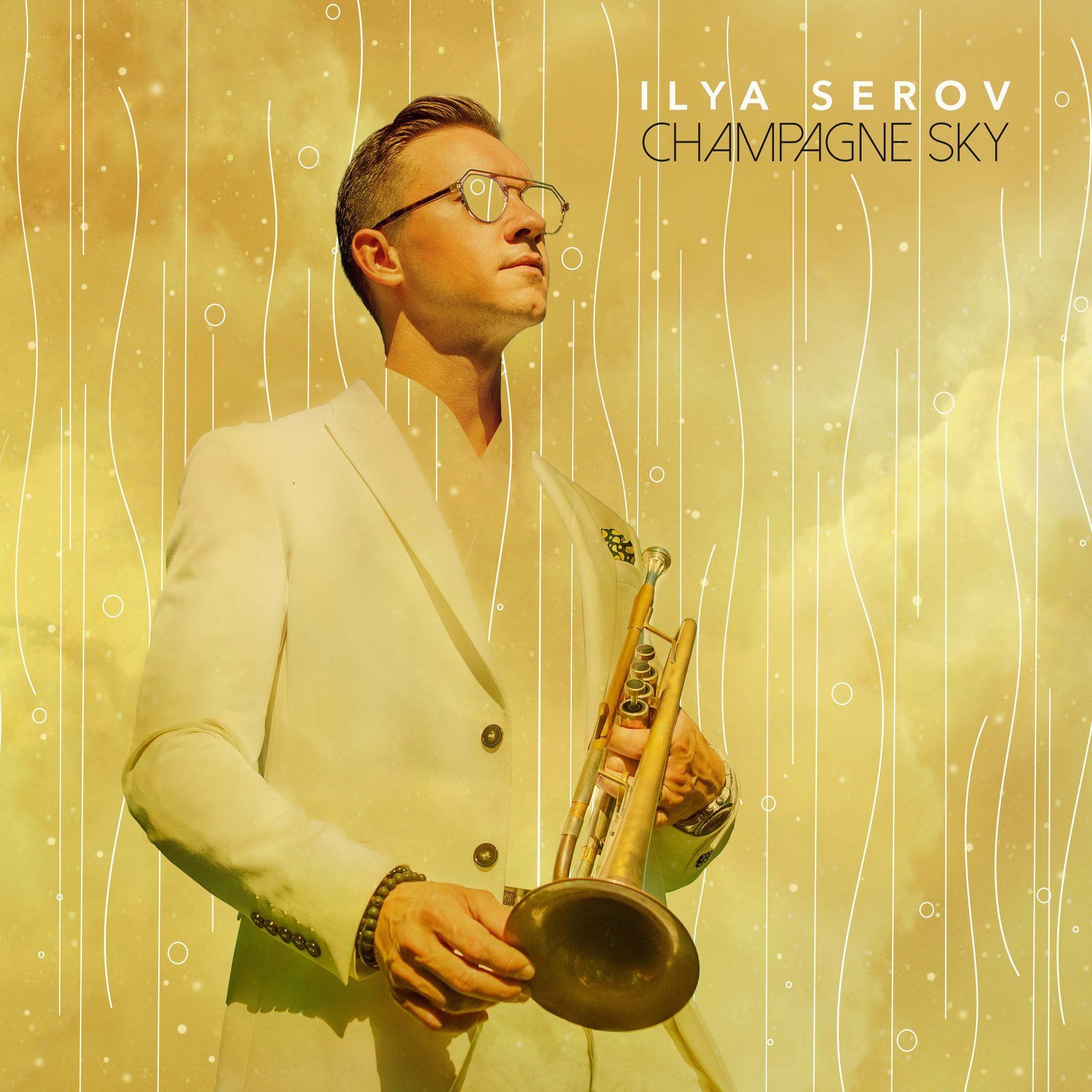Ilya Serov, a musician, holding a trumpet. He's wearing a white suit, looking up against a champagne-colored background.