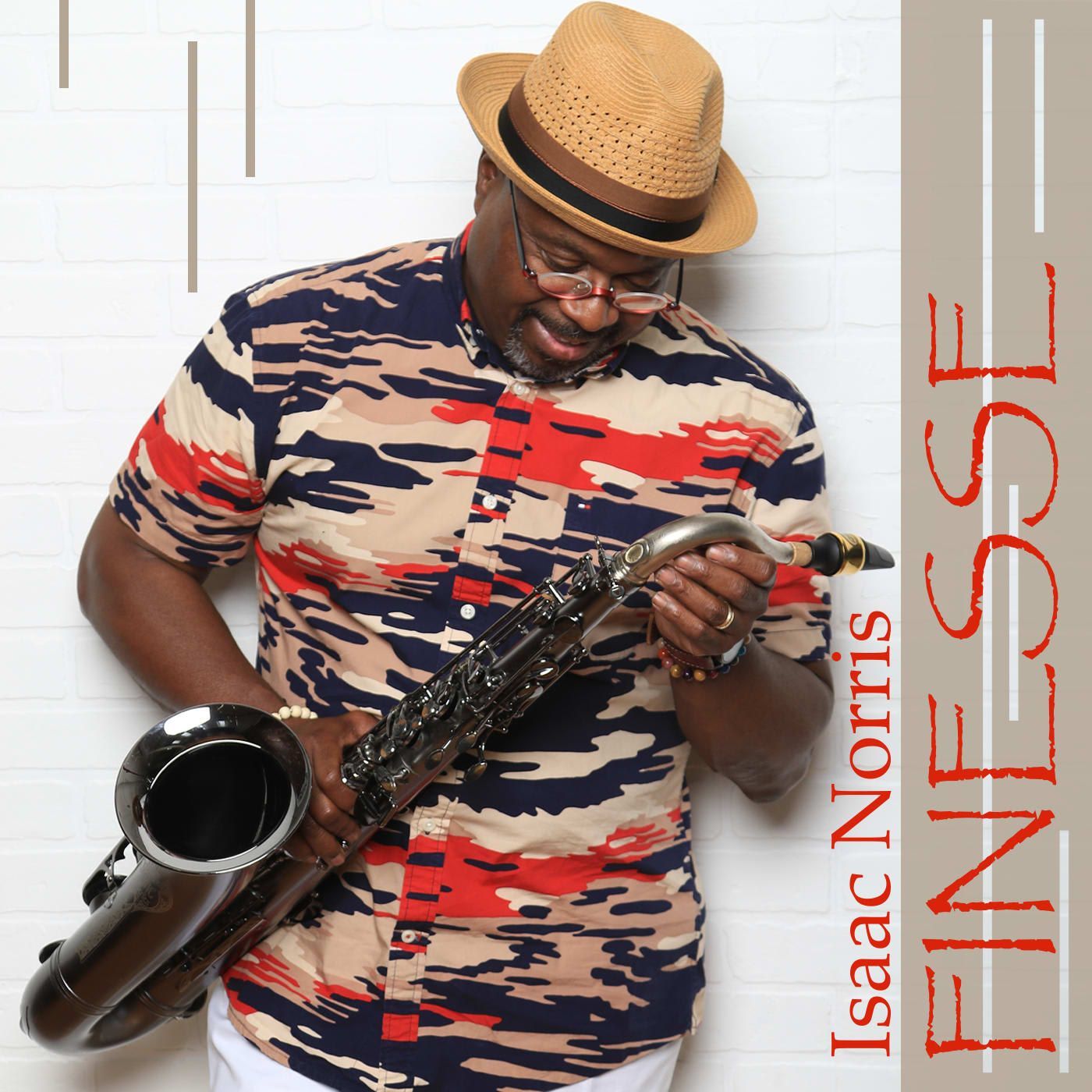 Saxophonist Isaac Norris holding a saxophone, wearing a patterned shirt and hat, in front of a white wall.