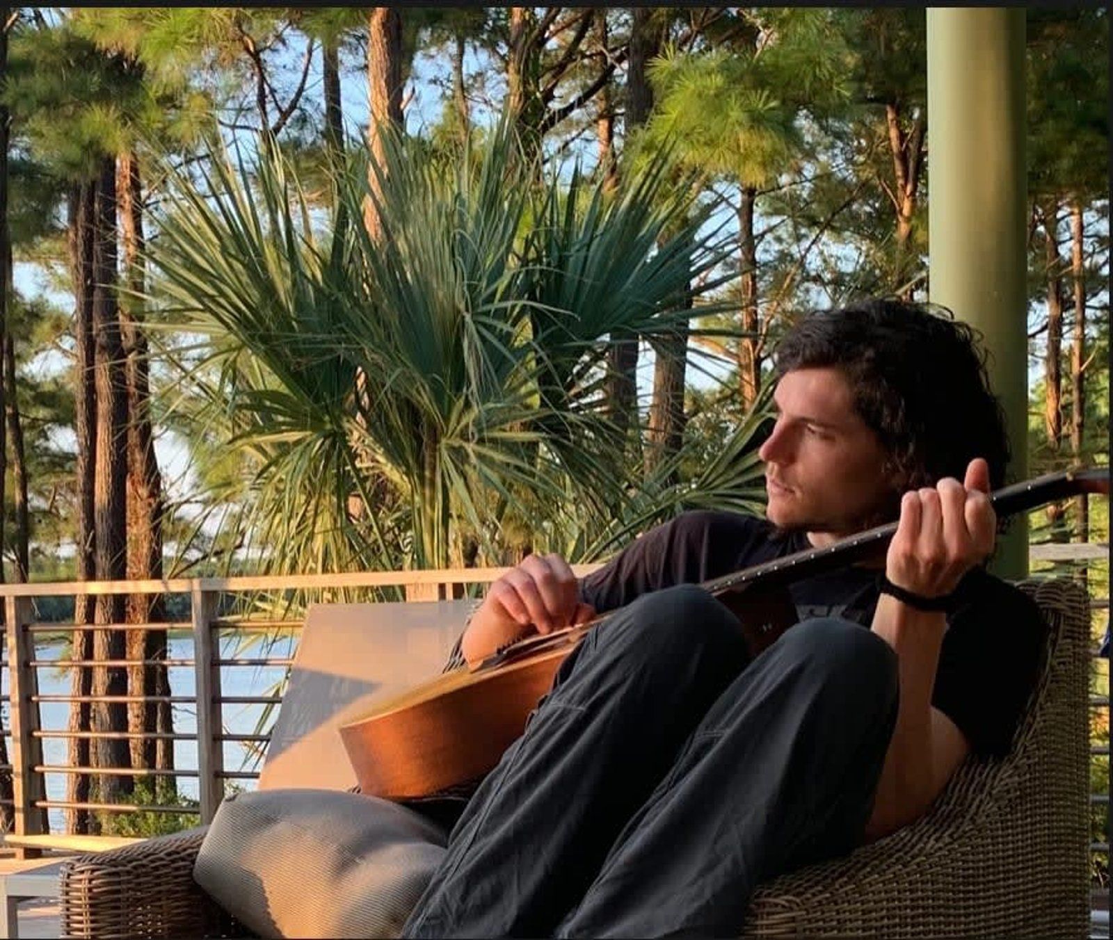 Man playing acoustic guitar outdoors, backlit by sun.