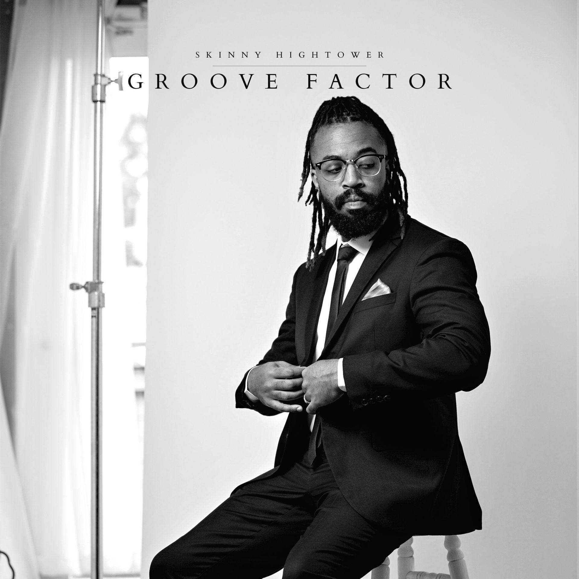Black and white photo of a man, in a suit, sitting, looking down. Text: 