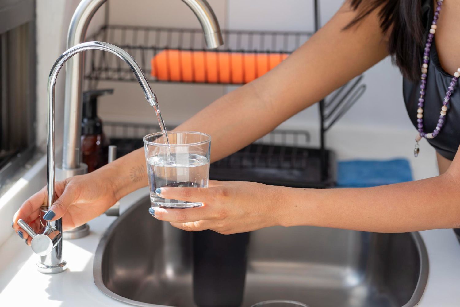 A woman is pouring water into a glass in a kitchen sink.