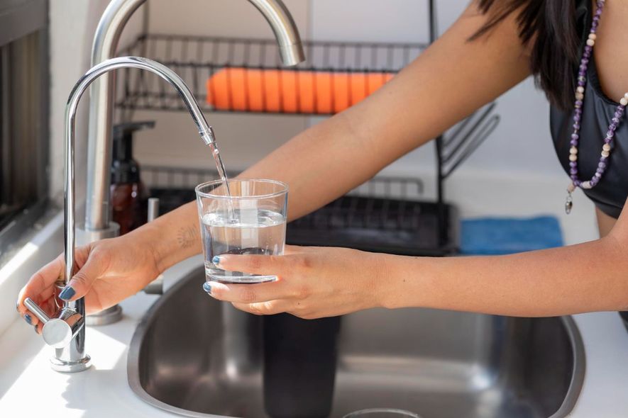 A woman is pouring water into a glass in a kitchen sink, water treatment systems
