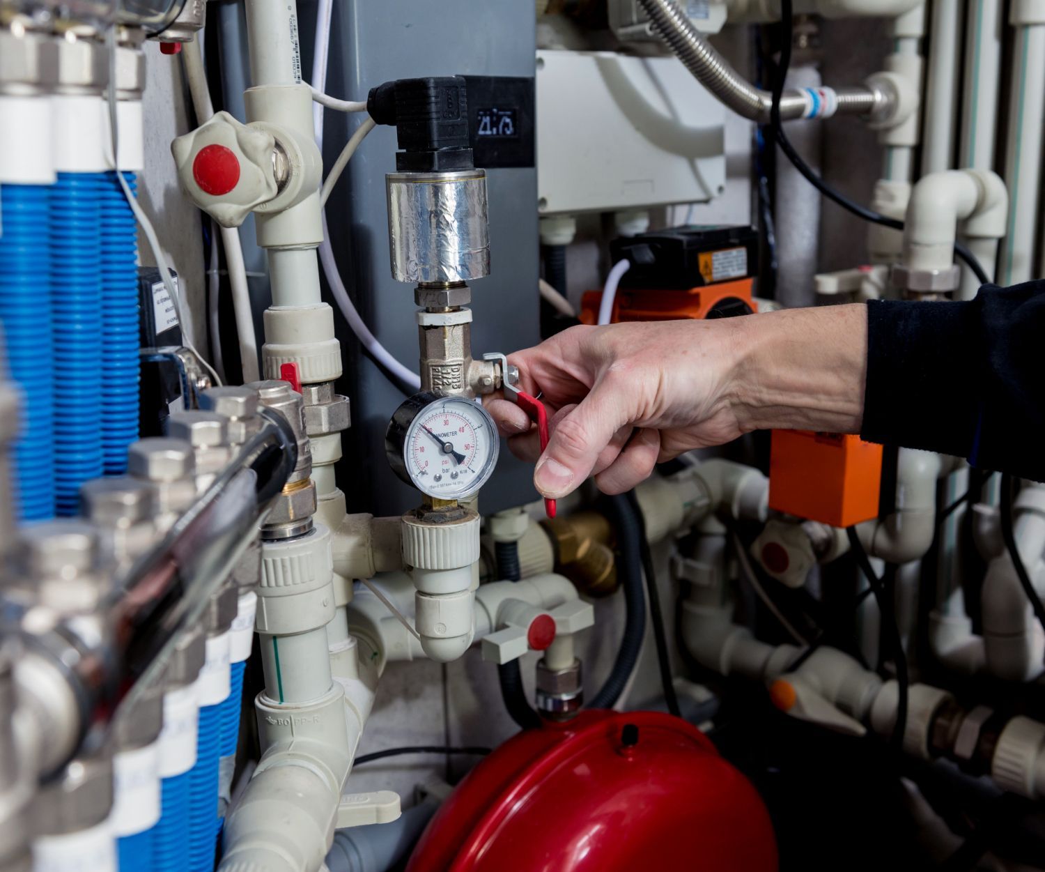 A person is adjusting a pressure gauge in a boiler room.