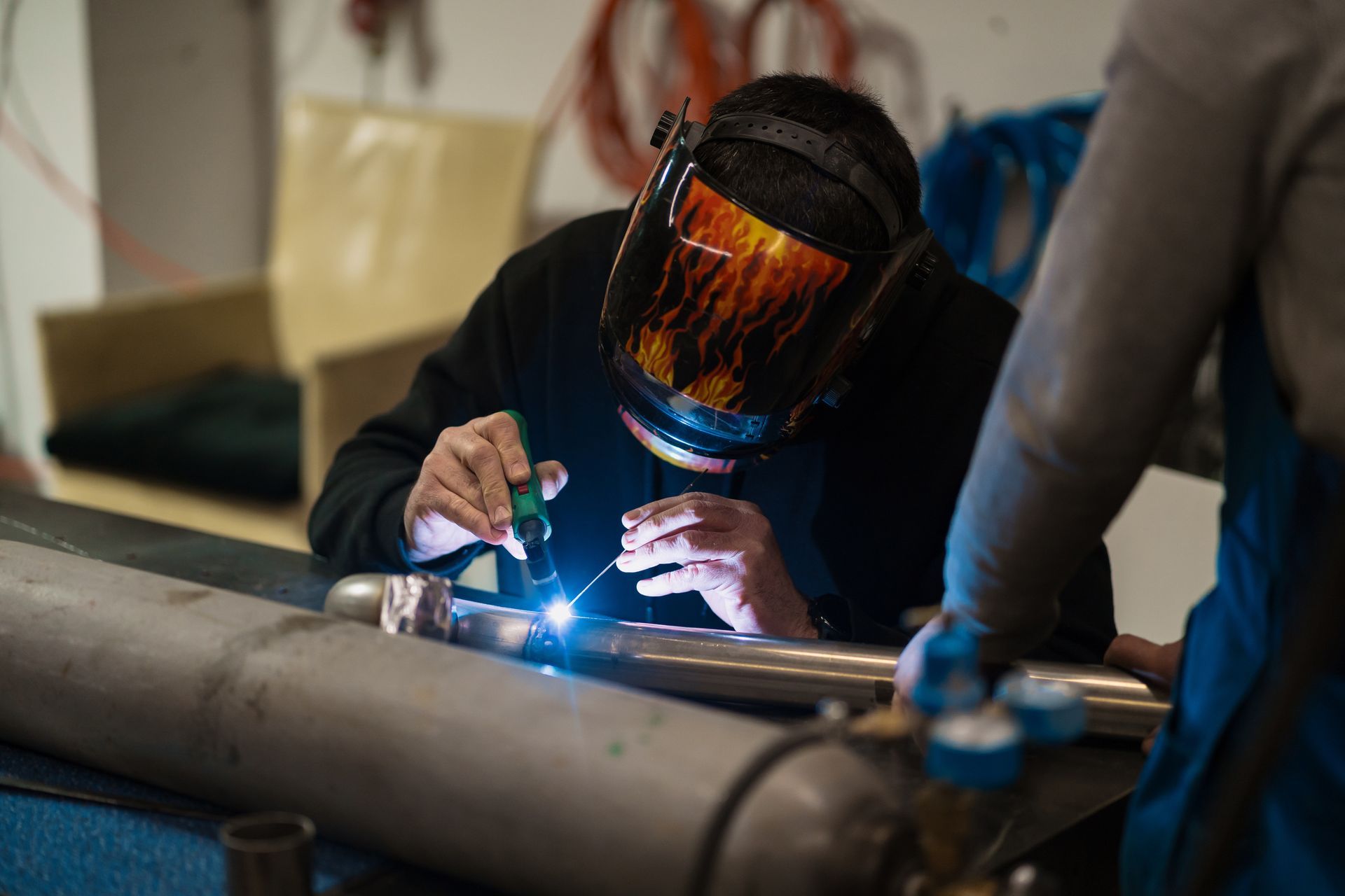 A man wearing a welding mask is welding a pipe.