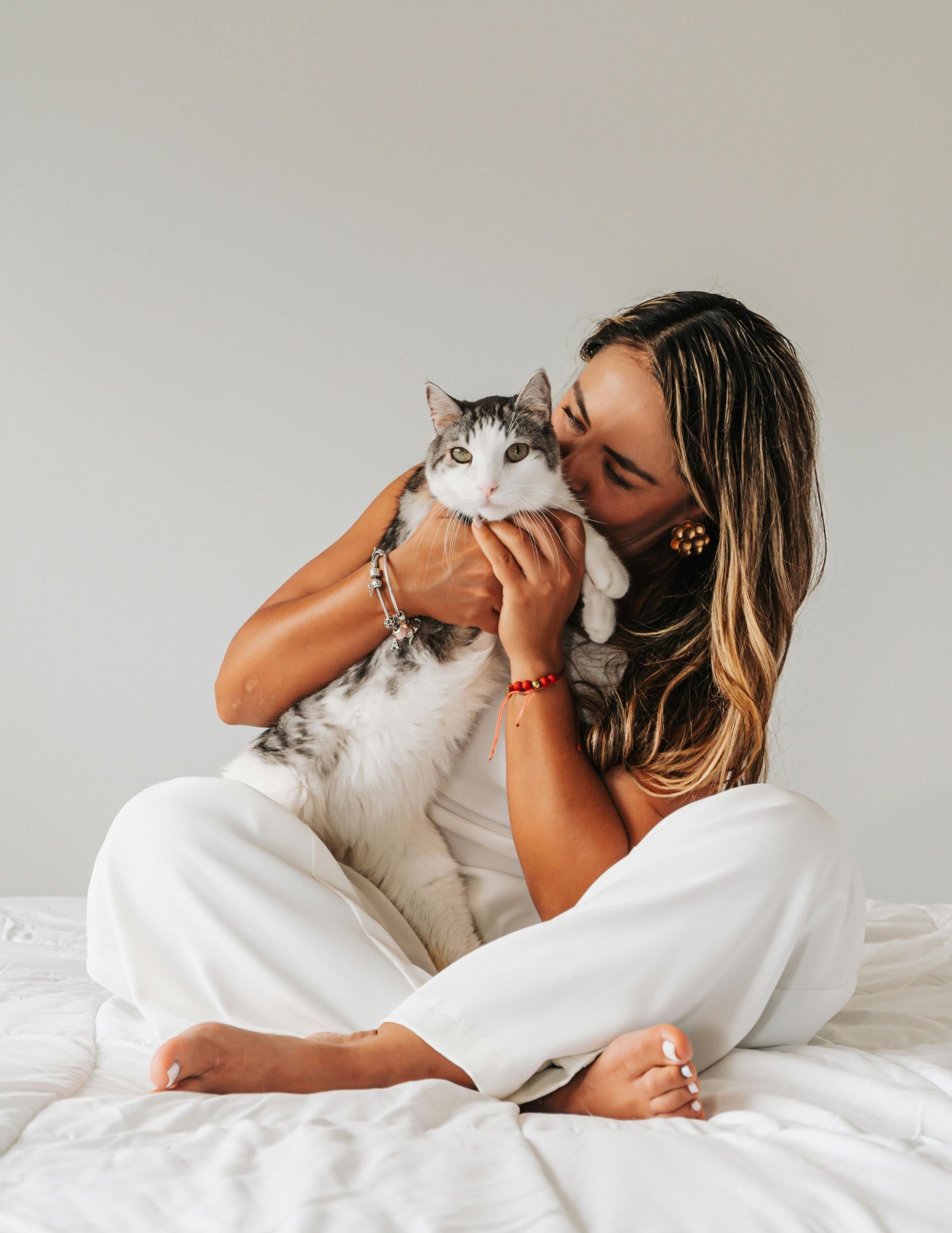 A woman is sitting on a bed holding a cat.