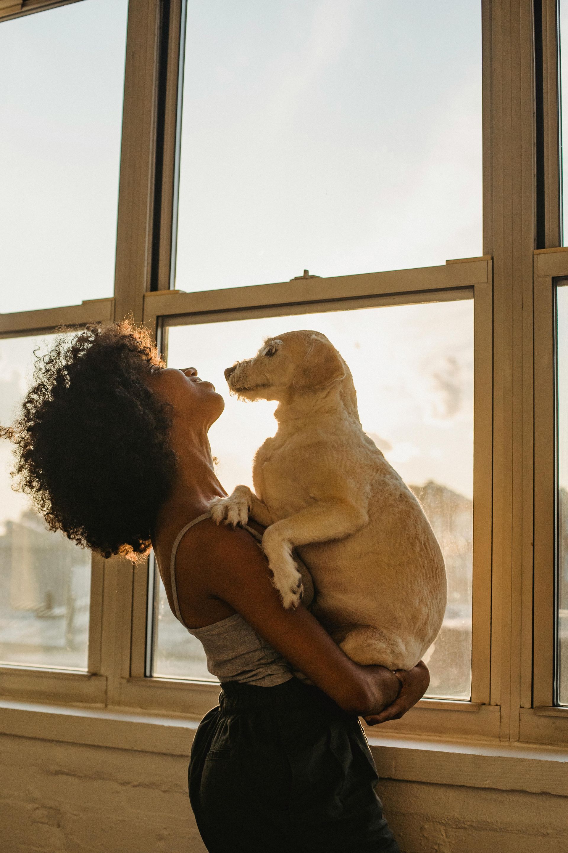 A woman is holding a puppy in her arms in front of a window.
