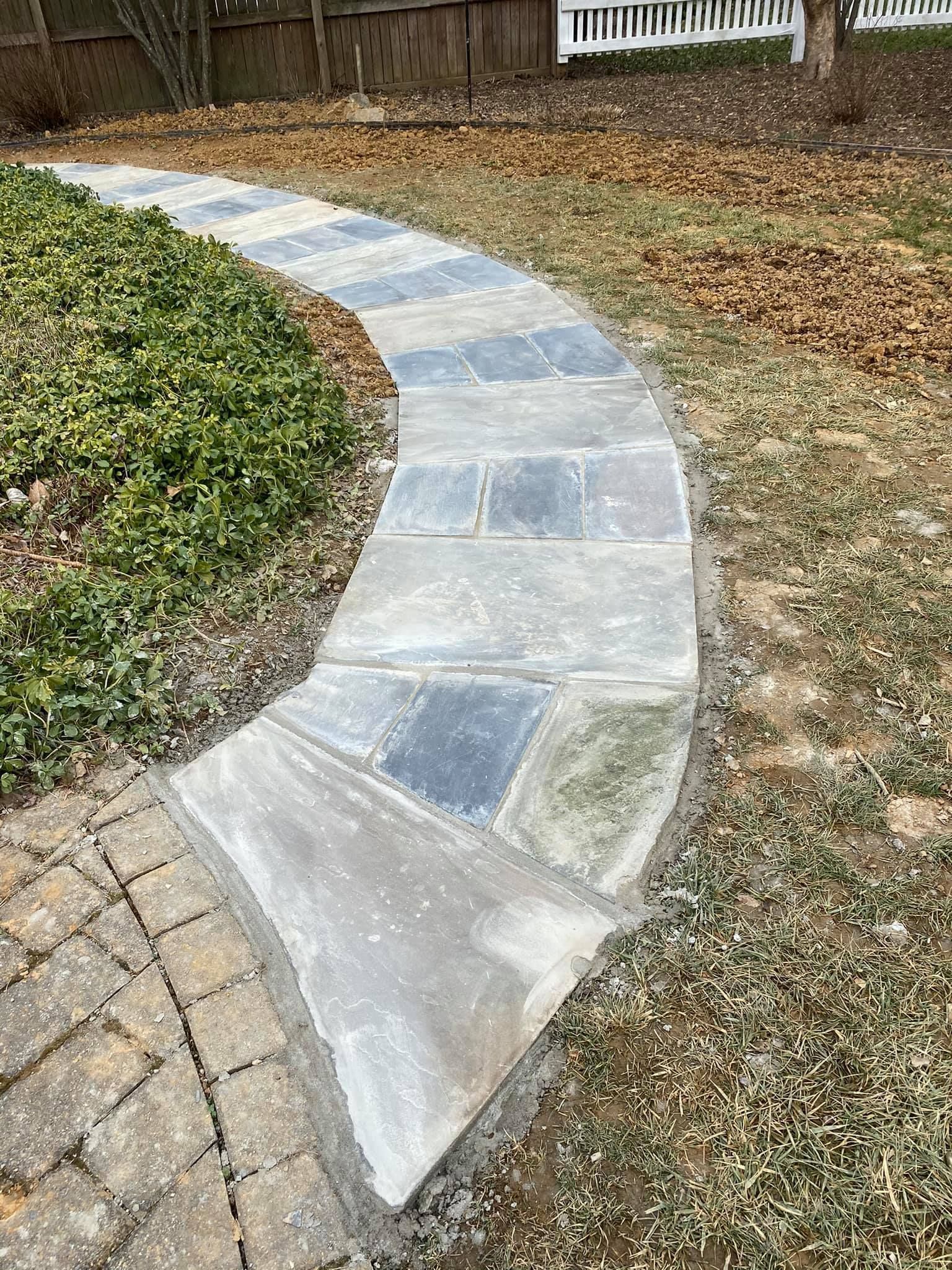 A concrete walkway going through a grassy area next to a fence.