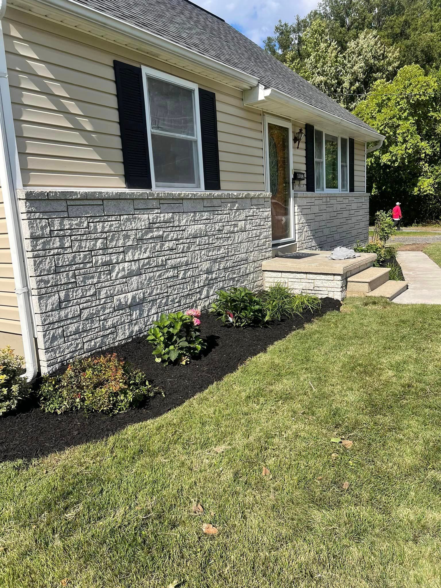 A house with a stone facade and black shutters is sitting on top of a lush green lawn.