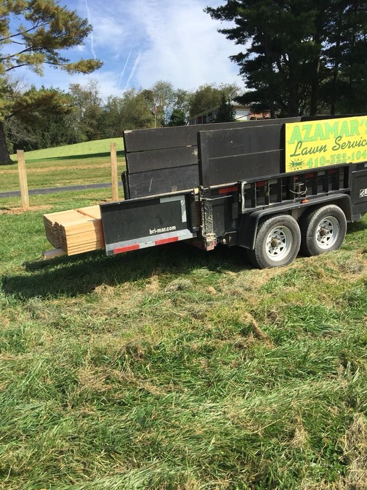 A black trailer with a yellow sign on the side is parked in a grassy field.