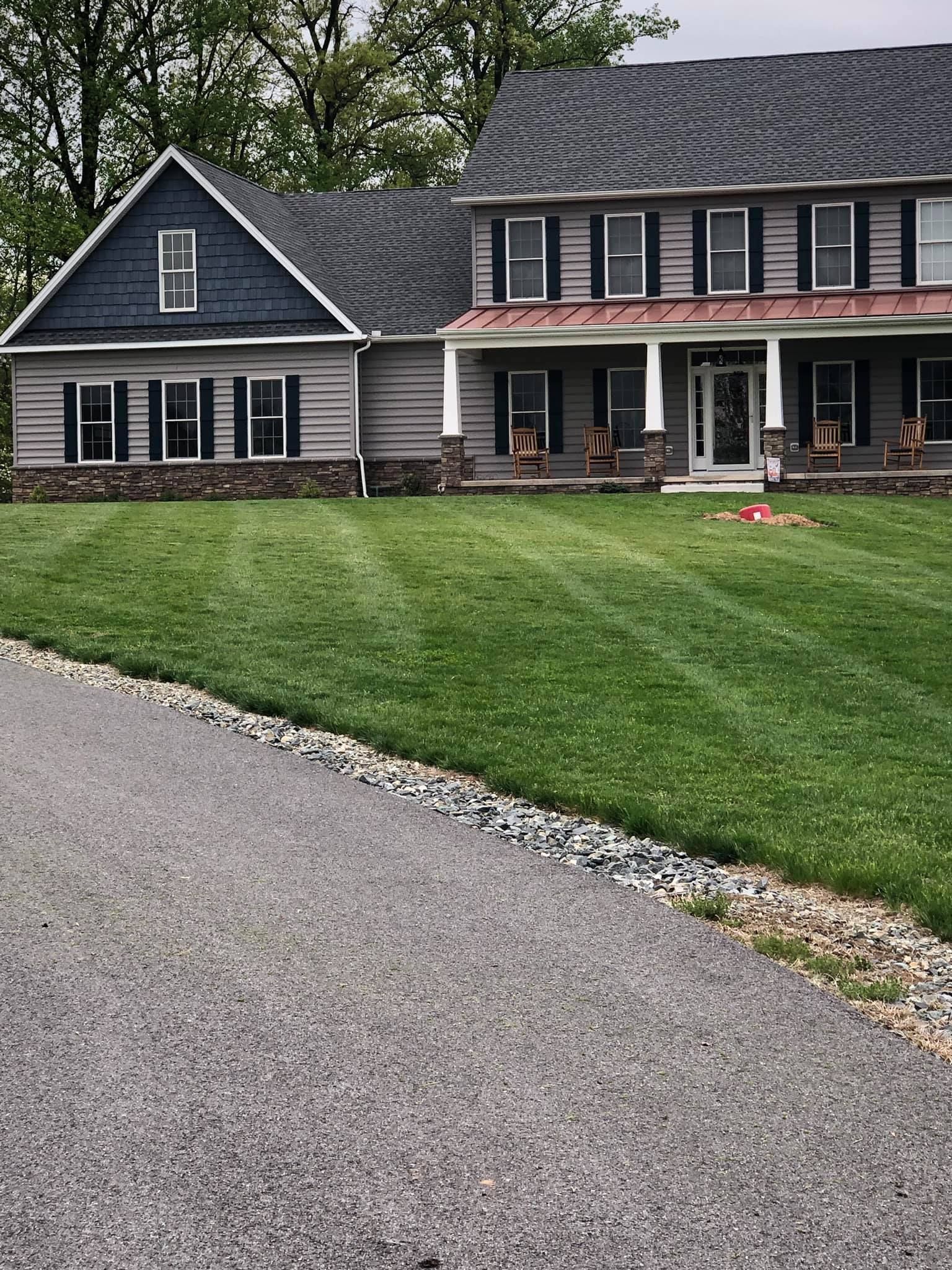 A large house with a lush green lawn and a driveway leading to it.
