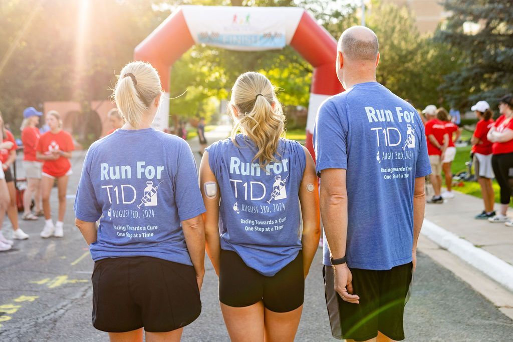 Mother, father, and T1D daughter with CGM on her arm, facing race start arch.