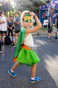 A little girl is wearing a green cape and mask.
