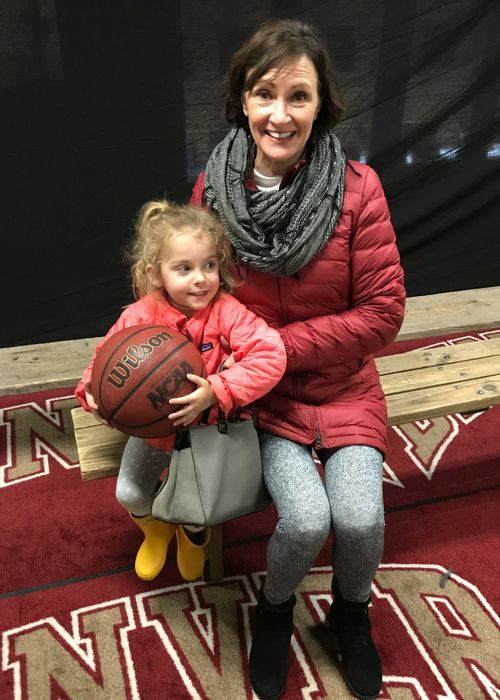 A woman is holding a little girl who is holding a wilson basketball