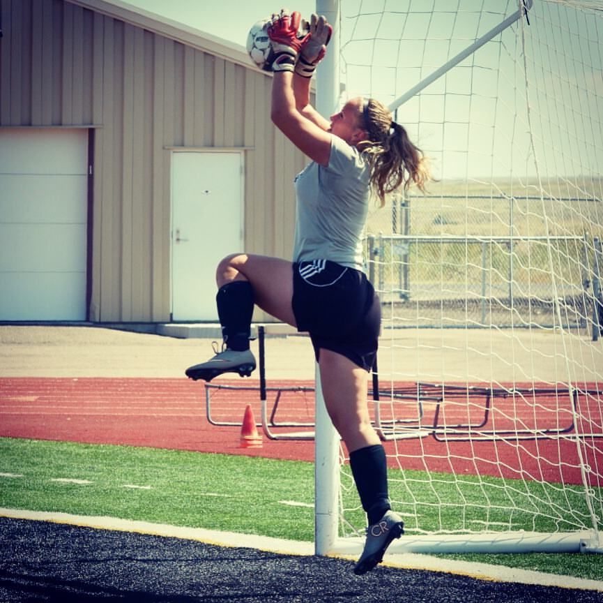 A female soccer player reaches up to catch a ball