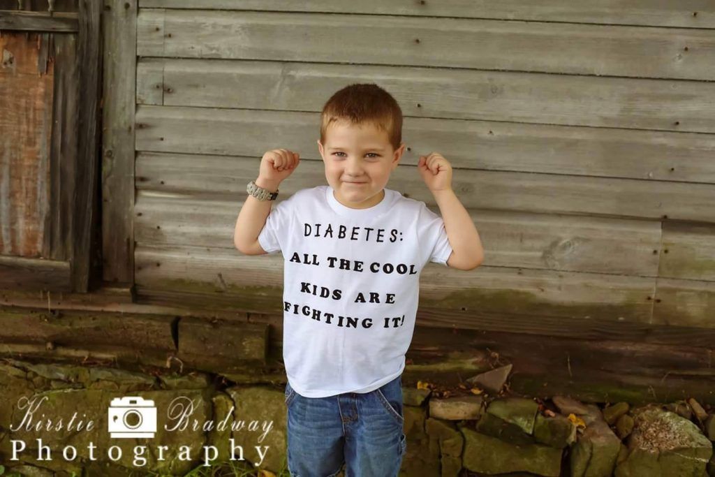 A young boy is flexing his muscles in front of a wooden wall.