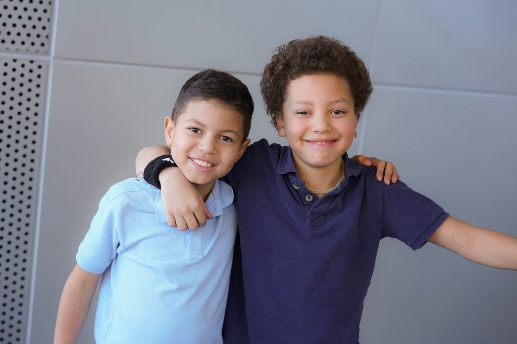 Two young boys are hugging each other and smiling for the camera.