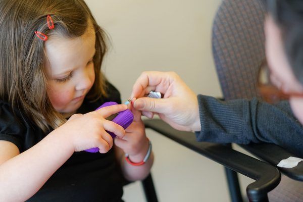 A little girl is getting her nails painted by a man.