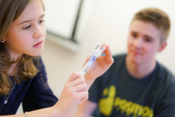 A girl holding a syringe next to a boy wearing a shirt that says solution