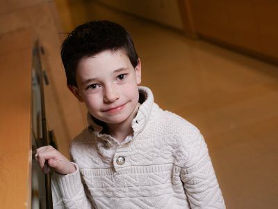 A young boy in a white sweater is standing next to a cabinet.