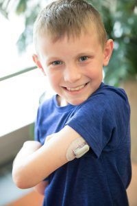 A young boy with a bandage on his arm is smiling.