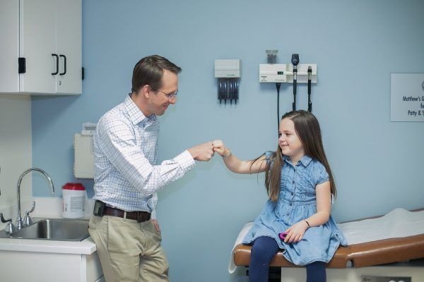 A man and a little girl are giving each other a high five in a doctor 's office.