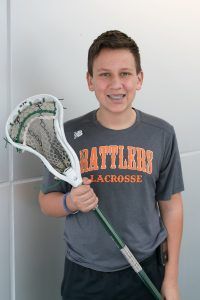 A young boy in a battlers lacrosse shirt is holding a lacrosse stick.