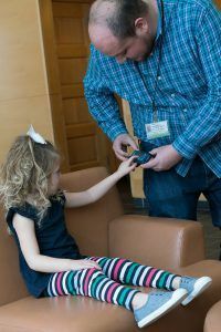 A little girl is sitting on a couch while a man holds her hand.